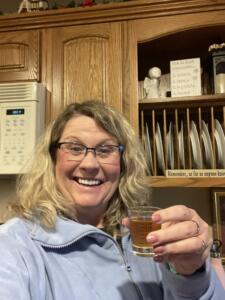 A smiley woman holding up a shot glass of Glow liquid collagen