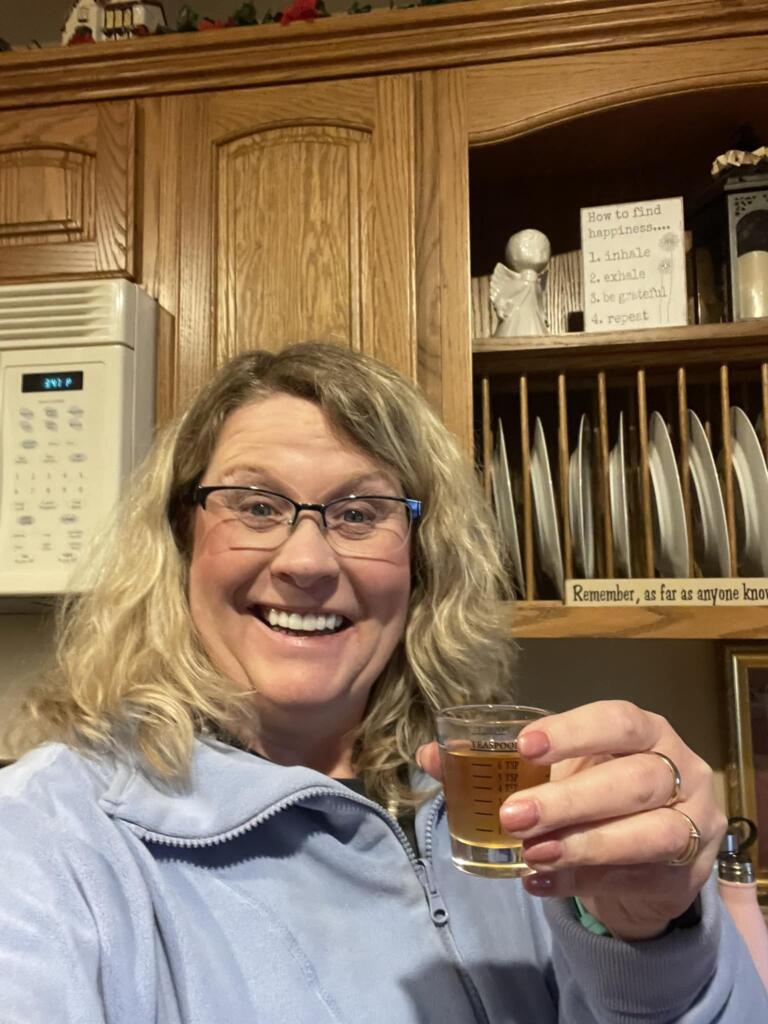 A smiley woman holding up a shot glass of Glow liquid collagen