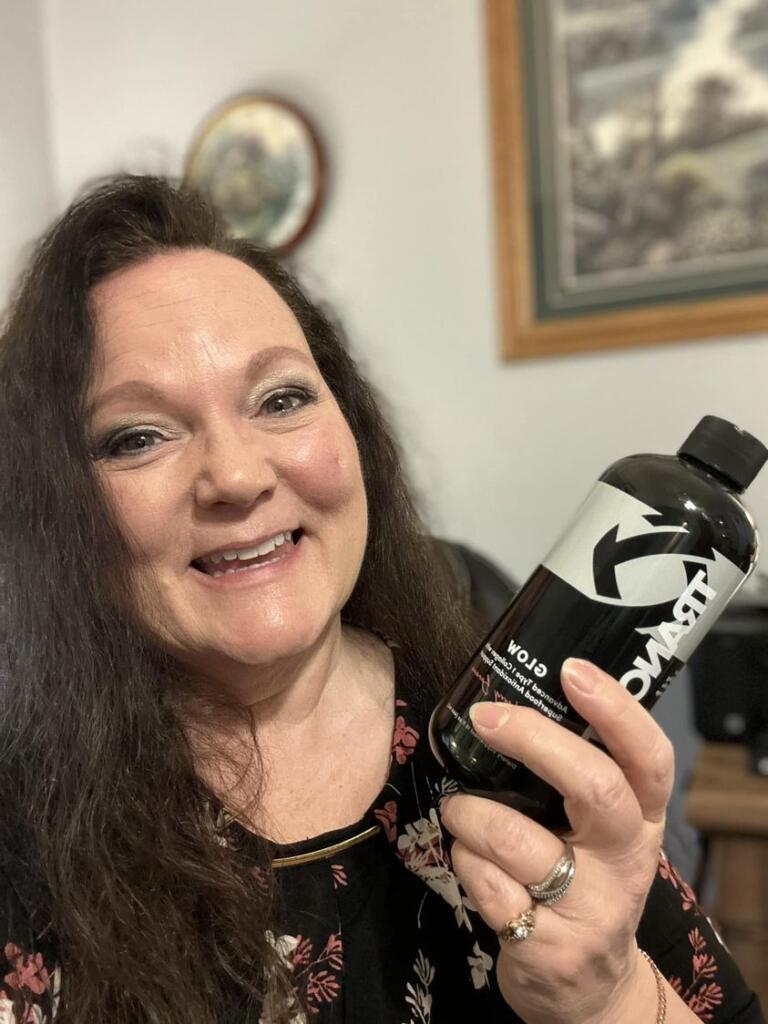 A very happy woman holding up a bottle of Glow collagen