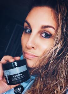 A woman holding up a bottle of Enrich